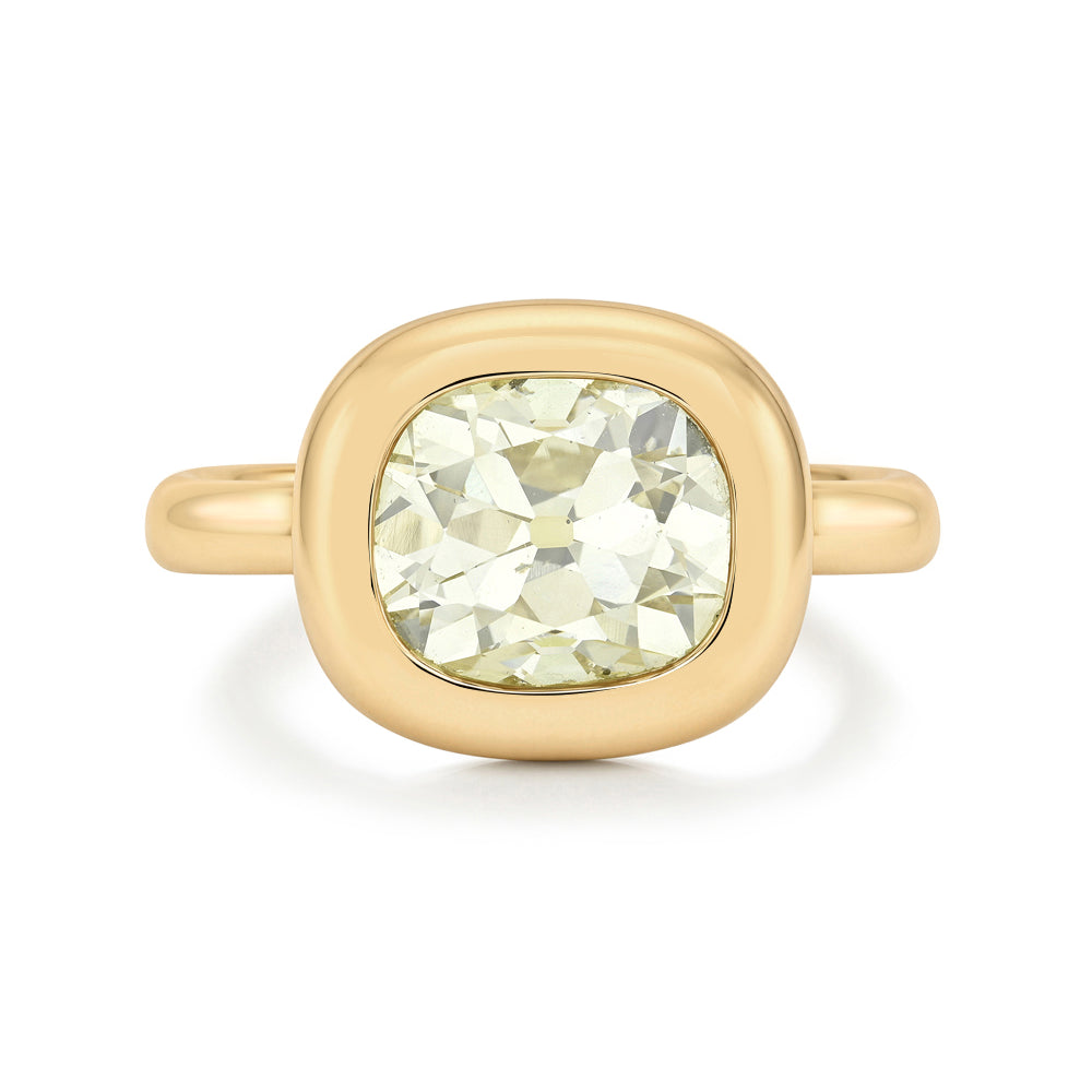 A gold ring featuring a large, cushion-brilliant cut pale yellow diamond in a rounded bezel setting, shown on a clean white background.