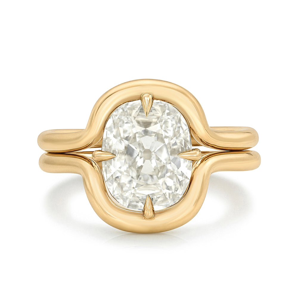 A yellow gold ring featuring a large cushion old mine-cut flat diamond in a prong setting, with a sculptural curved band design, shown on a clean white background.