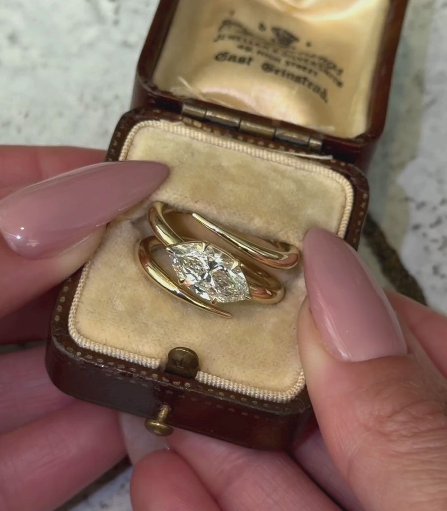14K yellow gold triple coil ring with a 2.01ct pear shaped brilliant cut champagne diamond set in a tilted orientation in a engagement ring setting shown in a box with hands.