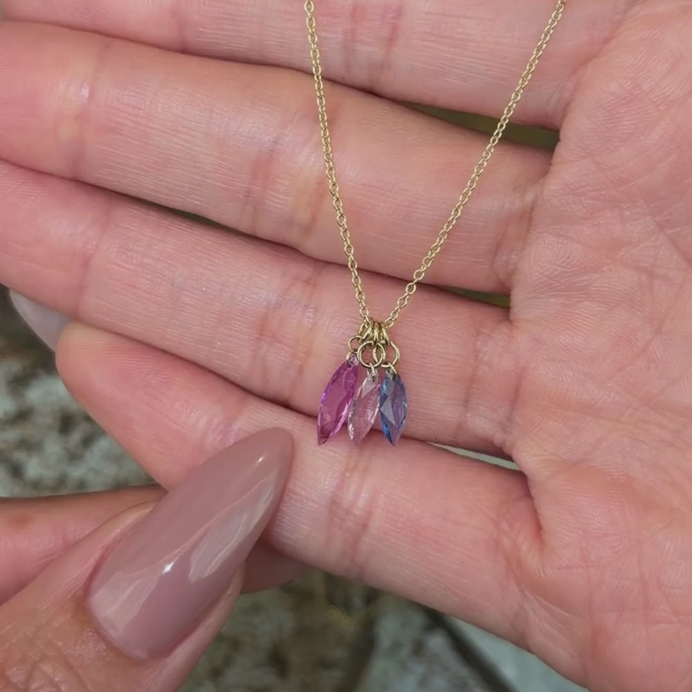 14K yellow gold chain necklace with three pear brilliant cut sapphire pendants in purple, pink and blue shown with hands.