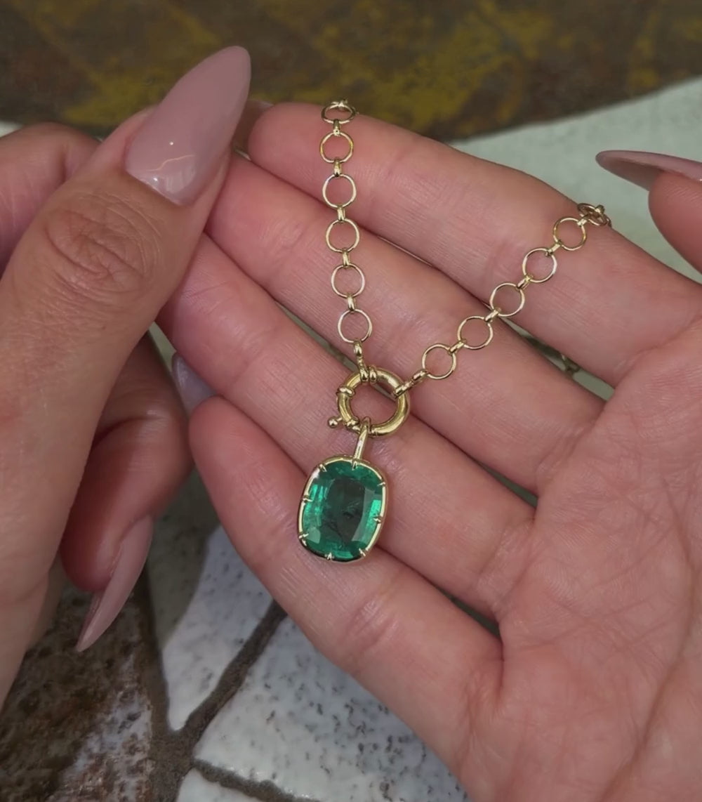 14K yellow gold loop chain necklace with an elongated cushion emerald pendant and spring ring closure shown with hands.