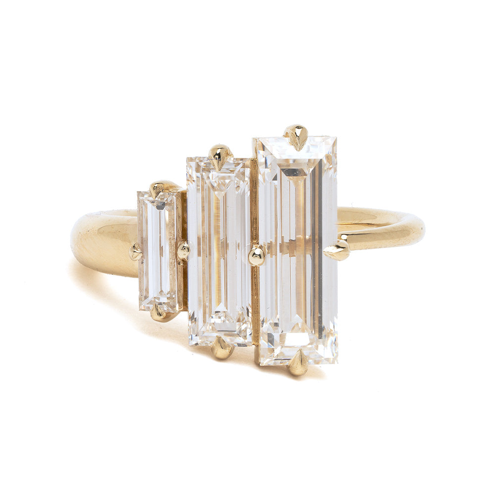 Gold ring with three emerald-cut diamonds on a white background