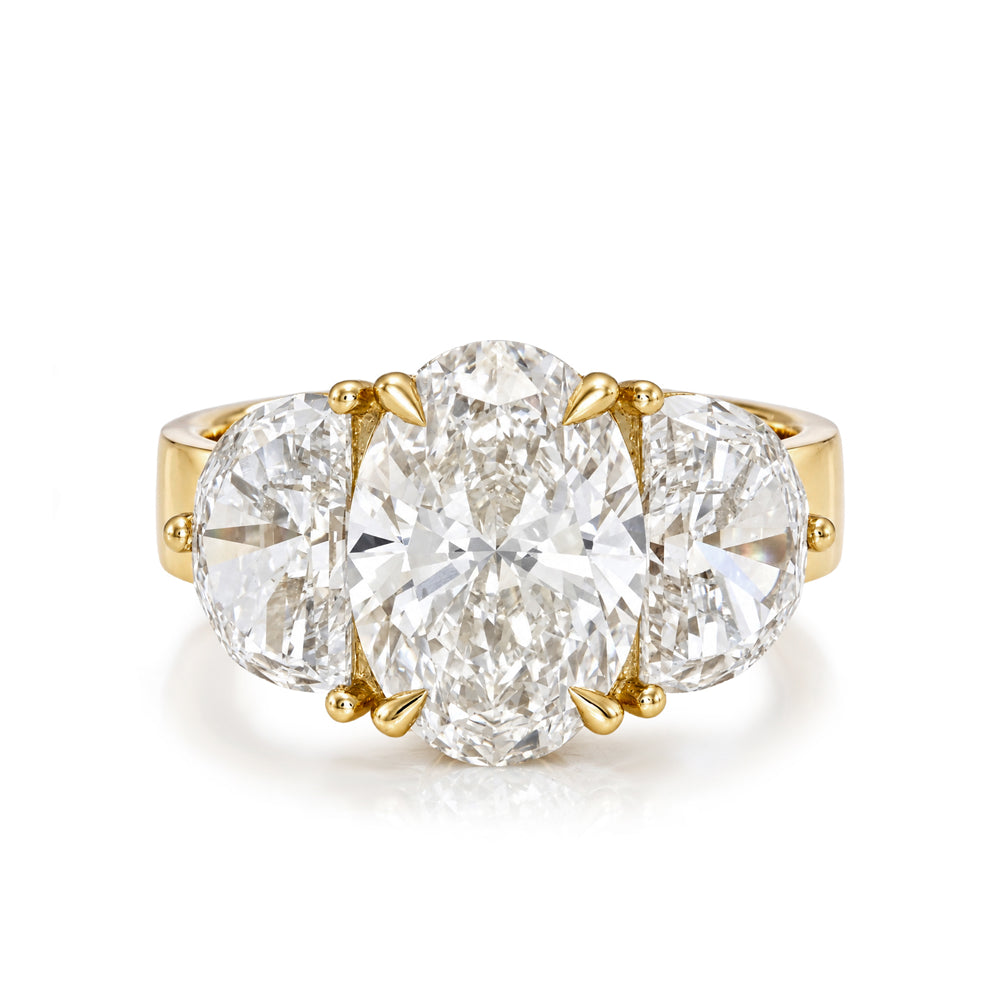 A yellow gold three-stone ring featuring a large oval center diamond flanked by two round side diamonds, set against a clean white background.
