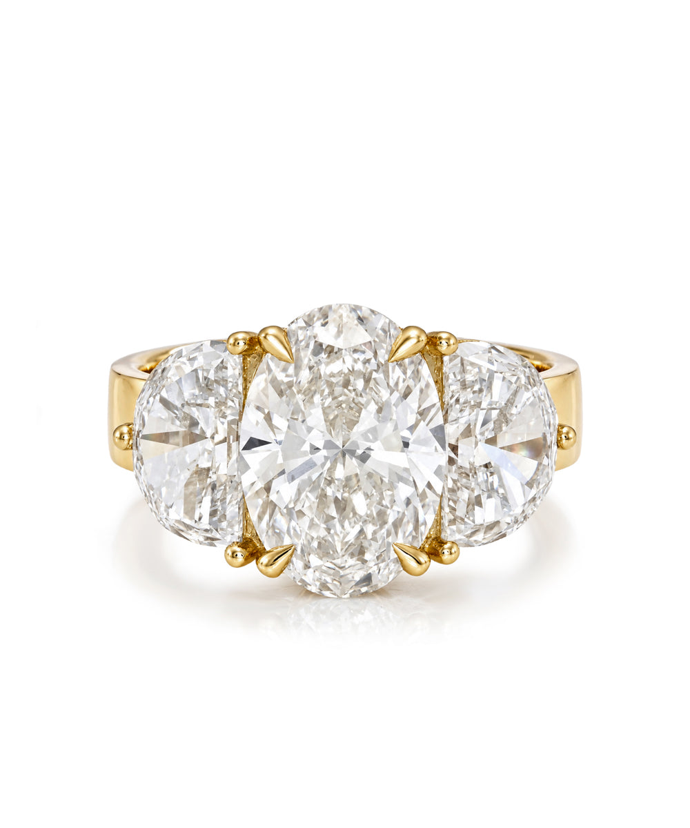 A yellow gold three-stone ring featuring a large oval center diamond flanked by two round side diamonds, set against a clean white background.