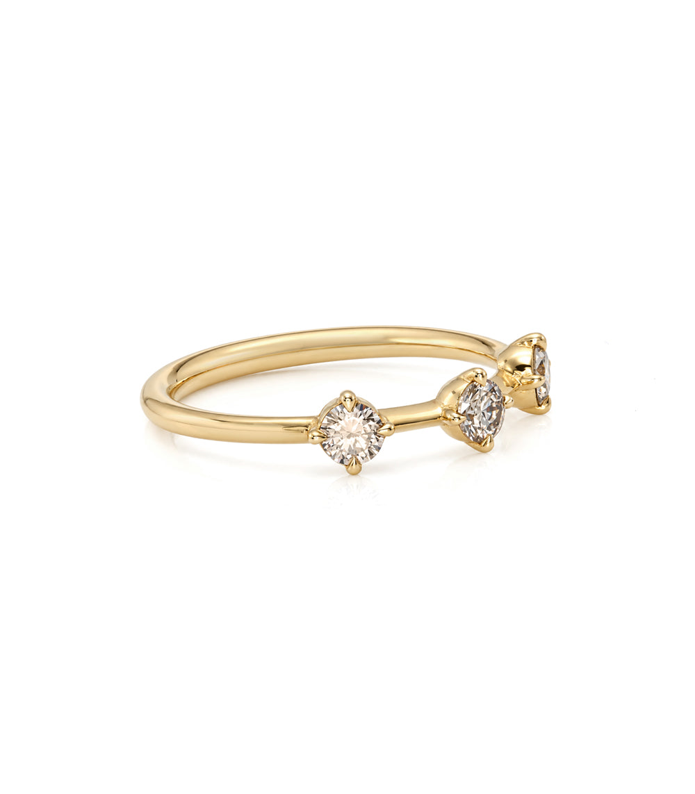 A delicate yellow gold ring featuring three small clear gemstones in a row, photographed on a clean white background.