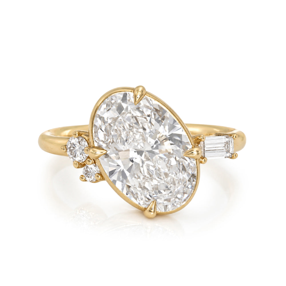 A yellow gold ring featuring a large oval-cut diamond center stone, accented by a small round diamond and an emerald-cut side diamond on a clean white background.