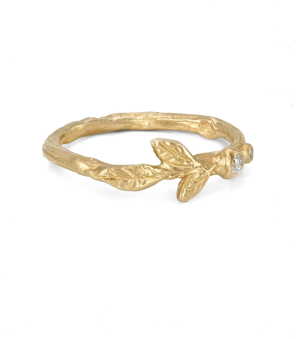 A textured yellow gold ring designed like a leafy branch, featuring a small clear gemstone at the tip, shown on a plain white background.