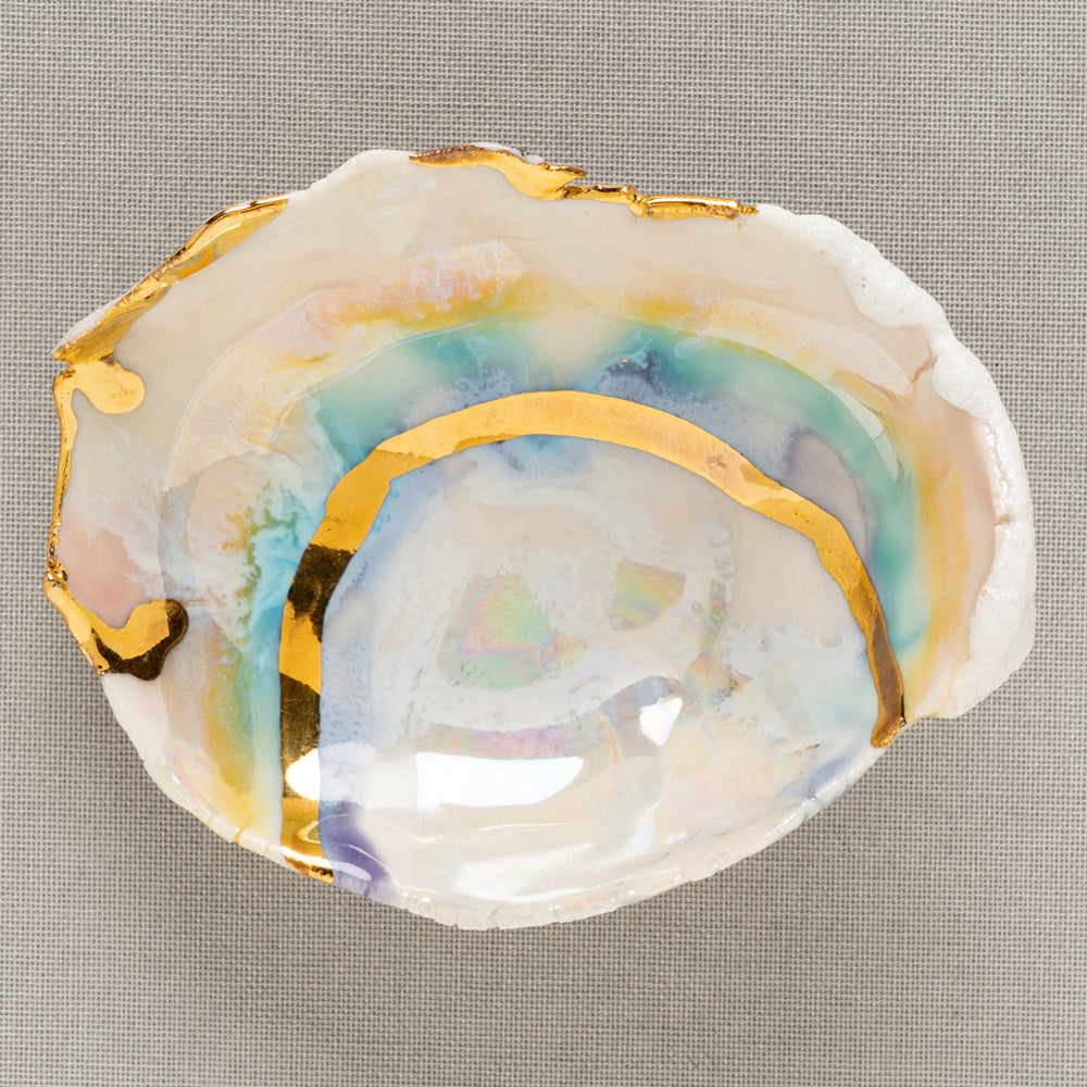 Mini Prism Ring Dish by G-004 shows an iridescent white dish with gold leaf edges on textured fabric.