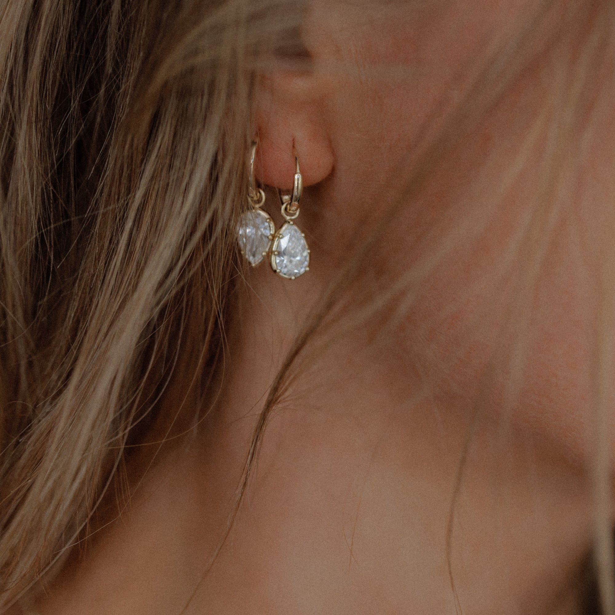 Womans Ear With 14k Yellow Gold Huggie Hoop Earrings With 1ct Diamond Drops